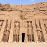 The colossal facade of the Great Temple of Ramesses II at Abu Simbel, carved into a sandstone cliff, with four massive seated statues of the pharaoh guarding the entrance